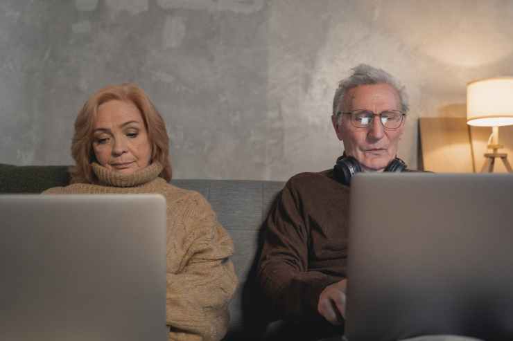 elderly man and woman sitting on couch using laptop computers